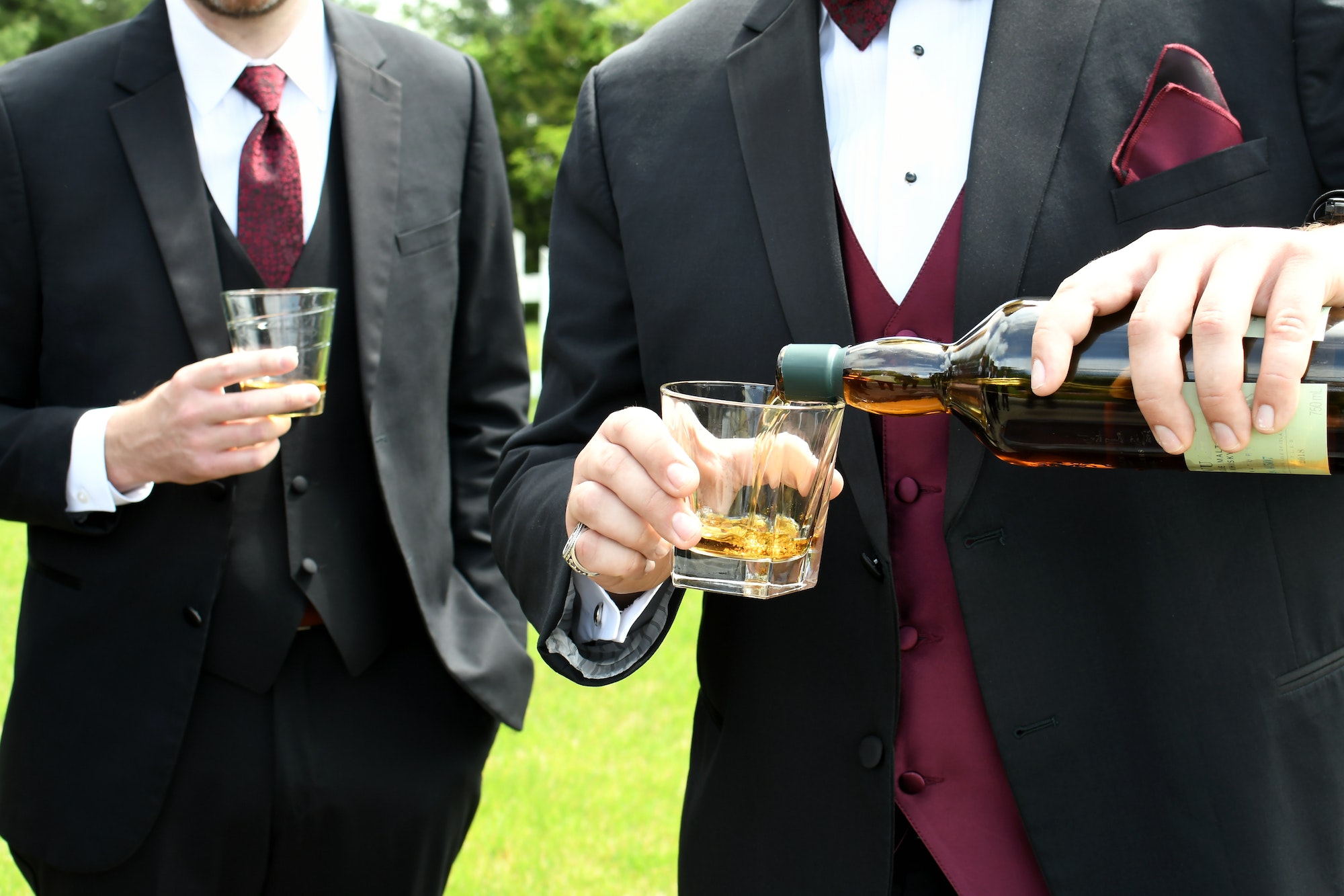 A man groom in a tux tuxedo pouring scotch into a glass for his groomsmen.