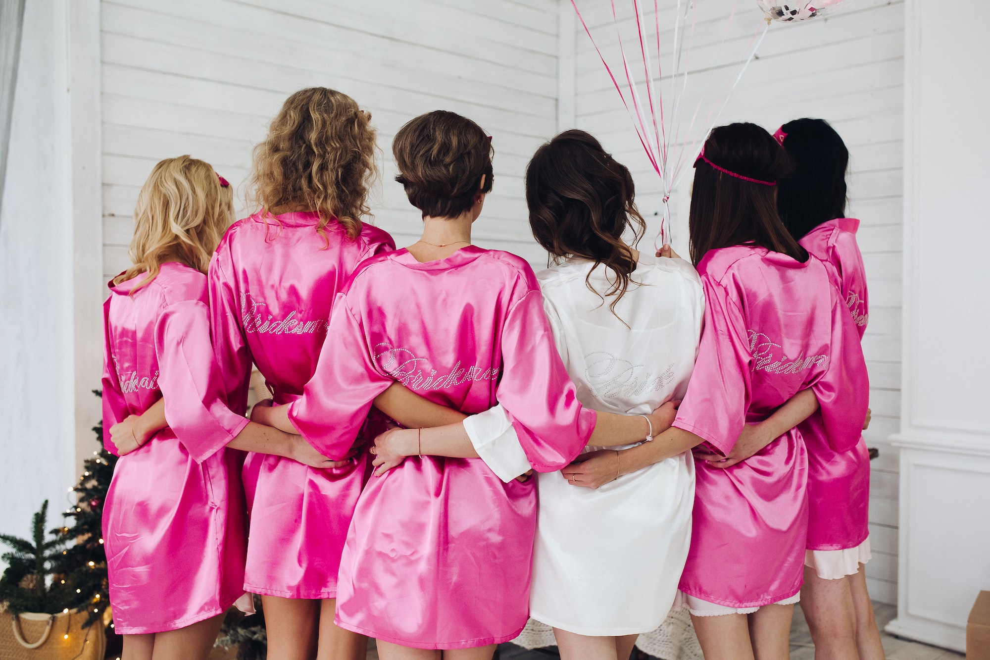 Bridesmaids in pink silk robes with the word 'bridesmaid' on bac