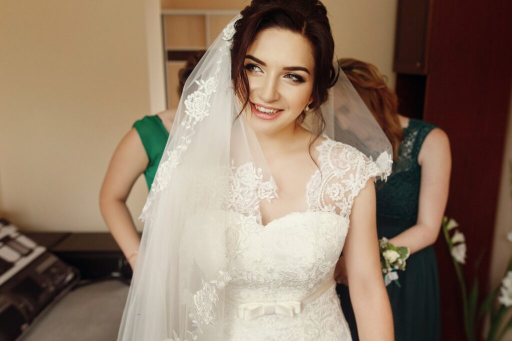 Stylish beautiful bridesmaids helping gorgeous brunette bride in white dress